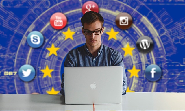muž, který pracuje na počítači, v pozadí za sebou má znak EU a okolo znaky sociálních sítí atd.
